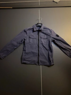 Blå overshirt med dragkedja - Snygg blå overshirt från Stone Island. Den är köpt på NK för cirka ett år sedan. Kan tänkta mig gå ner lite i pris för en snabb affär.