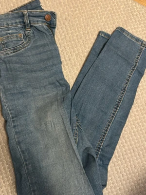 Blå skinny jeans från Gina tricot - Säljer ett par klassiska blå skinny jeans från Gina tricot med normalhög midja. Jeansen har 2 fickor, dragkedja och knapp framtill. Perfekta till alla dina outfits!