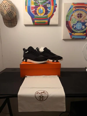 Svarta H sneakers med vit sula - Säljer ett par svarta H sneakers med chunky vit och svart sula. Skorna har en modern design med snörning och detaljer i mocka och textil. Kommer med original orange box och dustbag. Perfekta för dig som vill ha något exklusivt och stilrent. Pris kan diskuteras!!