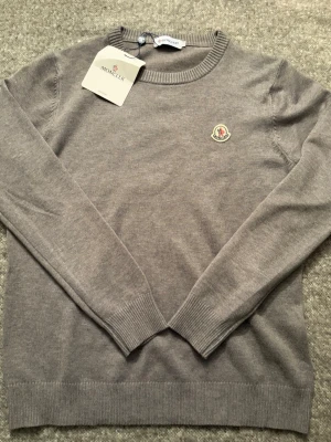 Grå stickad tröja från Moncler - Snygg grå stickad tröja från Moncler med rund halsringning och Moncler-logga broderad på bröstet. Fin tröja perfekt nu till våren och kallare sommardagar fr endast 499, pris kan diskuteras vid snabb affär✅