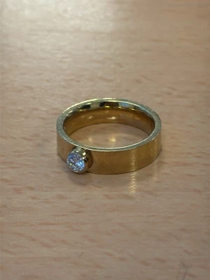 Guldfärgad ring från Edblad med klar sten - Snygg guldfärgad ring med bred, slät ring och en stor klar sten infattad framtill. Ringen har en modern och stilren design som verkligen sticker ut. Perfekt för dig som gillar statement-smycken och vill ha något som syns. Den är från Edblad och har storlek 17.5