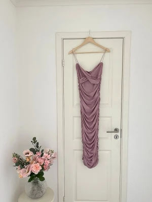 Ljuslila midiklänning Oh Polly - Säljer en elegant och feminin Oh Polly-klänning i vacker mauve lila nyans. Klänningen är i midi-längd och tillverkad i ett mjukt, stretchigt material som formar sig fint efter kroppen och ger en smickrande timglasform.  Den har tunna spaghettiband och dragkedja i ryggen för perfekt passform. Storlek UK 10, tack vare det stretchiga materialet passar den både S och M.  Klänningen skickas i sin originalförpackning och är i mycket fint skick. Endast använd en gång.