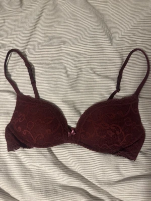 Vinröd push up bh från Intimissimi - Säljer en vinröd bh från Intimissimi med vacker spets och liten rosett framtill. Justerbara axelband och hakknäppning bak. Push up. Inte helt säker på storlek men runt 70 B