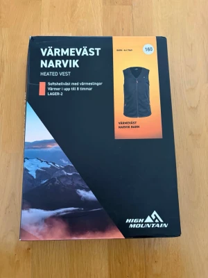 Värmeväst High Mountain Narvik Barn, Storlek 160 - Med denna värmeväst är ditt barn redo för alla vinteräventyr!  En stretchig och vattenavvisande värmeväst i softshell som håller barnet varmt trots bitande kyla. Utrustad med smarta värmeslingor och praktiska funktioner. Perfekt för utomhusaktiviteter under de kalla dagarna.  En värmeväst som är designad för att hålla ditt barn varmt under kalla dagar. Den är tillverkad i stretchig softshell som är vattenavvisande, vilket gör den perfekt för lek ute i alla väder. Västen har tre värmeslingor som 