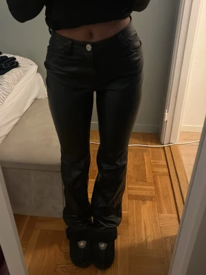 Svarta bootcut byxor i skinnimitation Bershka - Säljer ett par svarta byxor från Bershka i skinnimitation. De har hög midja, bootcut-ben och klassiska fickor både fram och bak. Snygg passform som sitter tajt upptill och släpper vid ankeln. 