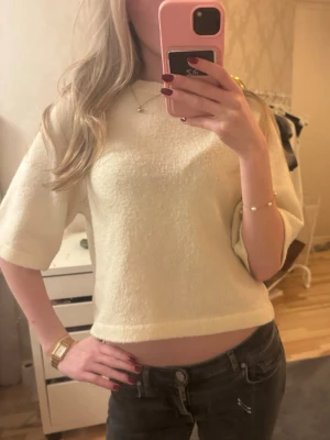 Vit kortärmad stickad topp - Vit croppad stickad topp – stilren och mjuk Denna topp är croppad med halvlånga ärmar och har en enkel, tidlös design. Materialet är mjukt och härligt mot huden, vilket gör den superbekväm att bära. Trots sin oversize-passform är den kort i modellen, vilket skapar ett snyggt mellanrum mellan tröjan och byxorna och framhäver silhuetten på ett avslappnat sätt. (Storlek 134 - 140 , men sitter som xs)