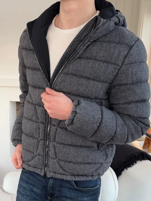 Grå pufferjacka från Herno i ull storlek 50 - Säljer en grå pufferjacka från Herno med huva och dragkedja framtill. Jackan har quiltad design, långa ärmar och två sidofickor med dragkedja. Perfekt för kyligare dagar och riktigt skön att bära. Passar dig som gillar en clean och modern look.