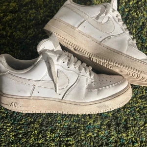 Nike Air Force 1 vita sneakers 44.5 - Klassiska Nike Air Force 1 sneakers i helvitt skinn med perforerad tå, rund tå och platt sula. Snygg low-top modell med snörning och ikonisk Swoosh-logga på sidorna. Perfekta för dig som gillar streetstyle och vill ha en tidlös sneaker i garderoben. Box medföljer