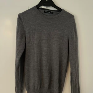 Grå stickad tröja från J.Lindeberg - Snygg grå stickad tröja från J.Lindeberg i klassisk modell. Tröjan har rund halsringning, långa ärmar och diskret logga på bröstet. Perfekt för lager-på-lager och passar till allt. Tillverkad i mjukt material som känns skönt mot huden.