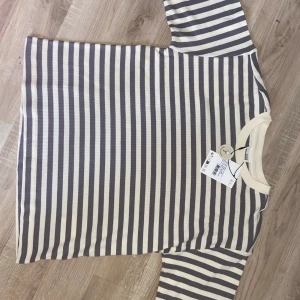 Randig t-shirt från Sofie Schnoor - Superfräsch t-shirt från Sofie Schnoor i ekologisk bomull. T-shirten har breda horisontella ränder i grått och vitt, rund halsringning och en loose fit. Perfekt för dig som gillar en chill och stilren look. Nypris: 449