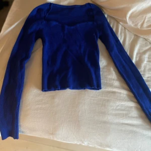 Kornblå ribbad långärmad topp - Säljer en kornblå ribbad långärmad topp med figurnära passform. Toppen har en lätt croppad längd och rundad halsringning. Perfekt att styla med jeans eller kjol för en snygg look.