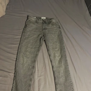 Grå jeans från Jack & Jones - Säljer ett par grå jeans från Jack & Jones i modellen Relaxed Chris. Jeansen har klassisk femficksdesign, bälteshällor och knappgylf. De är raka i modellen och har en avslappnad passform, perfekta för en chill och stilren look.
