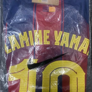 FC Barcelona Lamine Yamal matchtröja Nike S - FC Barcelona matchtröja med Lamine Yamal och nummer 10 på ryggen. Tröjan är randig i blått och rött med gula detaljer, Nike-logga och Spotify som sponsor. Tillverkad i Dri-FIT-material för bästa komfort. Officiell FCB-produkt.