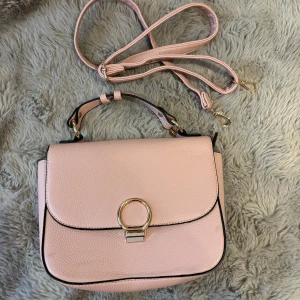 Ljusrosa axelväska med gulddetaljer - Ljusrosa axelväsk som har både handtag och lång rem så du kan bära den på flera sätt. 