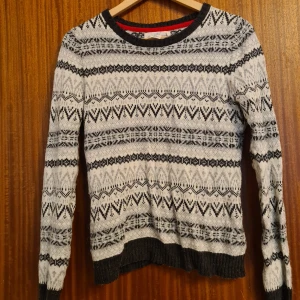 Mönstrad stickad tröja från L.O.G.G. - Säljer en stickad tröja från L.O.G.G. i svart och vitt med snyggt grafiskt mönster. Tröjan har rund halsringning, ribbade muddar och lång ärm. Perfekt för kalla dagar när du vill vara både varm och stilren. 