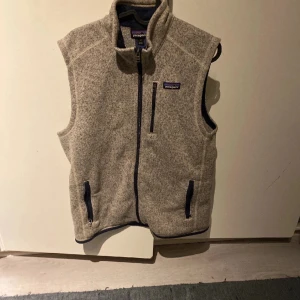 Beige fleeceväst från Patagonia - Tja! Säljer min Patagonia väst i ett mycket fint skick på grund av att den är för liten | Storlek på västen är M men den sitter som S | västen är sydd  från armhålan och ner till midjan på båda sidorna, alltså parallellt | Den passar dig som är 175-185 cm lång och väger ca 50-65 kg | Det låga priset är pga att västen är sydd, annars har den inga defekter | Den är perfekt nu till hösten, passar bra att ha under vinterjackan också | Hör av er vid eventuella frågor! 