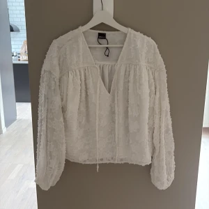 Vit blommig blus från Gina Tricot - Superfin vit blus från Gina Tricot i transparent tyg med blommiga detaljer. Blusen har långa puffärmar, v-ringning och knytband framtill. Perfekt för dig som gillar romantisk och luftig stil.