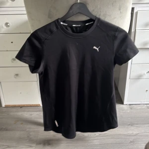 Svart Puma t-shirt i sportig stil - Svart t-shirt från Puma med klassisk logga på bröstet. Sportig design med rund hals och korta ärmar, perfekt för en aktiv vardag. Tillverkad i ett mjukt och lätt material som andas.