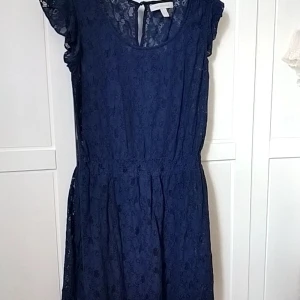 Marinblå spetsklänning Springfield - Snygg marinblå klänning från Springfield i spets med korta volangärmar och rund halsringning. Klänningen har markerad midja och är helfodrad förutom ärmarna som är transparenta. Perfekt för dig som gillar romantisk stil och vill sticka ut.