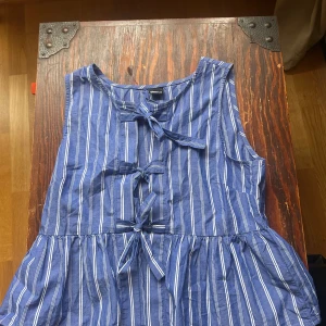 Blåvit randig blus Gina Tricot - Superfin blå klänning med vita ränder från Gina Tricot. Ärmlös modell med flera knytningar framtill och lätt utställd kjol. Perfekt för varma dagar och har en luftig känsla tack vare bomullsmaterialet.