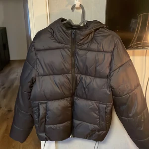Svart pufferjacka från Gina Tricot XS - Säljer en svart pufferjacka från Gina Tricot i storlek XS. Jackan har huva, stora fickor och dragkedja framtill. Perfekt för kalla dagar och har en snygg, boxig passform som är riktigt trendig just nu. Som har ett litet riv märke.