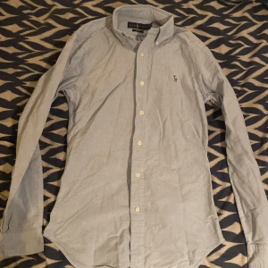 Slim fit skjorta från Ralph Lauren XS - Klassisk ljusblå skjorta från Ralph Lauren i slim fit-modell. Skjortan har långa ärmar, knappar framtill och ikonisk broderad logga på bröstet. Tillverkad i bomull och passar perfekt för en clean och stilren look. Kan förekomma katthår.