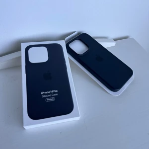 iPhone 14 Pro Silicone Case MagSafe - Original Apple iPhone 14 Pro Silicone Case med MagSafe. Fodralet är svart och skyddar din telefon effektivt. Viss slitage syns, särskilt ett tydligt märke i ett hörn. Levereras i originalförpackning.