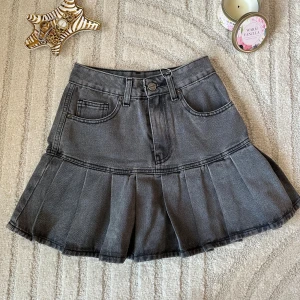 Grå jeanskjol med volang - Snygg grå jeanskjol med volang nertill och klassiska fickor fram. Kjolen har hällor för bälte och en cool, lite tvättad look. Perfekt för dig som gillar en trendig och avslappnad stil.