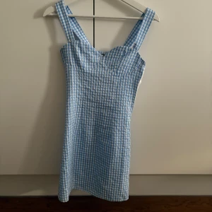 Blåvit klänning - Supersöt blåvit rutig klänning från H&M med breda axelband och smockad rygg. Klänningen är kort och har en figurnära passform med hjärtformad urringning. Passar både till vardags eller fest🦋