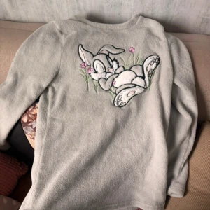 Disney fleece tröja med Kaninmotiv XS - Supermjuk ljusgrå fleece tröja från Disney i storlek XS. Tröjan har lång ärm och är perfekt för myskvällar. Matchande prickiga byxor finns också, men annonsen gäller för båda