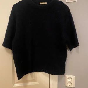 Svart stickad tröja från Gina Tricot - Mysig svart stickad tröja från Gina Tricot med rund hals och kortare ärmar. Perfekt för lager-på-lager och enkel att styla till olika outfits. Tröjan har en klassisk, lite loose passform och är superenkel att matcha.