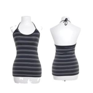 Randig svart halterneck linne - Snyggt svart linne med tunna vita ränder och halterneck-knäppning. Toppen har en tight passform och är ärmlös, perfekt för en stilren och enkel look. Materialet känns mjukt och stretchigt, vilket gör den bekväm att bära hela dagen.