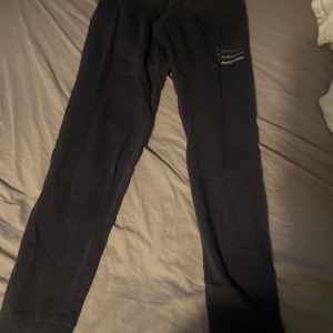 Svarta mjukisbyxor Peak Performance 160 - Svarta mjukisbyxor från Peak Performance i storlek 160. Byxorna har resår och snörning i midjan samt ribbade muddar vid bensluten. Perfekta för chill eller träning, med diskret logga på benet.