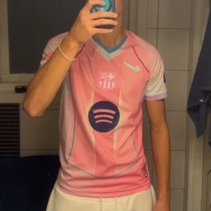 Rosa bara Barça tröja  - Säljer en rosa FC Barcelona fotbollströja från Nike med Lamine Yamal och nummer 10 på ryggen. Tröjan har korta ärmar, blå detaljer, sponsorlogga från Spotify och Champions League-märke på ärmen. Tillverkad i lätt och ventilerande material.