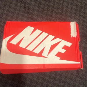 Nike Shox svarta sneakers med silverdetaljer - Nike Shox sneakers i svart med silvriga detaljer och den ikoniska fjädrande sulan. Ovandelen är i mesh och syntet med snörning och en sportig vibe. Swoosh-logga på sidan och cool design som sticker ut. Perfekta för dig som gillar streetwear och vill ha något unikt på fötterna.