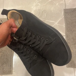 Christian Louboutin svarta sneakers mocka - Säljer ett par svarta sneakers från Christian Louboutin i mocka med klassisk röd sula och signaturdetalj undertill. Skorna har rund tå, svarta skosnören och svarta metalldetaljer. Insidan är i ljust skinn för extra komfort. Perfekt för dig som vill sticka ut med lyxig streetstyle.