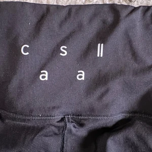 Svarta leggings från Casall - Säljer ett par svarta träningstights från Casall med stilren design och tryckt logga på midjan. De är tighta och har hög midja, perfekta för träning eller chill. Materialet är mjukt och stretchigt syntet som sitter skönt mot kroppen. Liten i storleken 