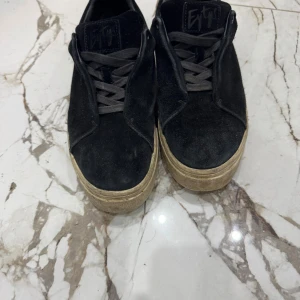 Svarta sneakers från Eytys i mocka - Säljer ett par svarta sneakers från Eytys med lila detalj på hälen och beige sula. Skorna har snörning och är gjorda i mocka med en klassisk rund tå. Perfekta för dig som gillar stilrena och trendiga sneakers med en twist.