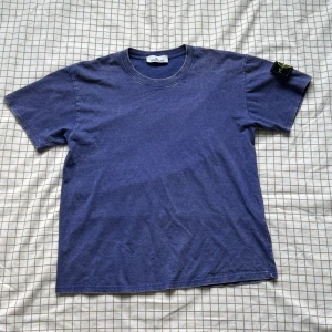 Blå Stone Island t-shirt i bomull - Säljer en blå t-shirt från Stone Island med klassisk rund hals och korta ärmar. T-shirten har en tvättad look och ikonisk Stone Island patch på vänster ärm. Tillverkad i mjuk bomull för skön känsla och stilren vibe.