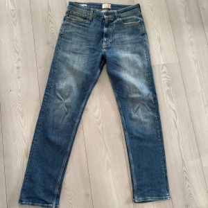 Blå jeans från Jack & Jones, stl 30/32 - Snygga blå jeans från Jack & Jones med klassisk femficksdesign och läderpatch bak. Jeansen har en rak passform och subtila slitningar framtill för en avslappnad look. Tillverkade i mjukt denimtyg som sitter skönt hela dagen. Finns en enda deffekt, det är insidan av benfickan så finns ett minimalt hål, detta syns såklart inte då det är insidan av fickan, kan knappt få in mitt lillfinger i hålet så litet det är men värt att nämna för allas bästa