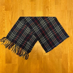 Mörkblå Burberry halsduk i lamull - Säljer en mörkblå Burberry halsduk i 100% lamull. Halsduken är i gott skick. Var inte rädd för frågor.