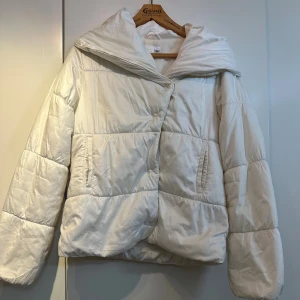 Vit pufferjacka, lättdunjacka från H&M - Säljer en snygg vit pufferjacka/lättdunjacka från H&M med stor krage. Inte supervarm så funkar perfekt nu i höst men man kan även ha den i vinter om man har tjockare kläder under