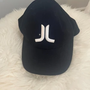 Svart keps från WESC med vit logga - Svart keps från WESC med böjd skärm och stor vit broderad logga framtill. Tillverkad i 97% bomull och 3% spandex för en bekväm passform. Perfekt för dig som gillar streetwear och vill ha en clean look.