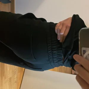 Svarta mjukisbyxor Stella från Lager 157 - Svarta byxor från Lager 157, modell Stella, med elastisk midja och dragsko. Byxorna har raka ben och sidfickor, vilket ger en chill och enkel look. Perfekta för dig som gillar bekväma och stilrena plagg.