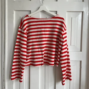 Randig röd och vit stickad tröja - Säljer en stickad tröja med röda och vita horisontella ränder. Tröjan har lång ärm, rak passform och en något croppad längd. Materialet är mjukt och luftigt stickat, perfekt för lager-på-lager. Båtringad hals ger en avslappnad vibe.