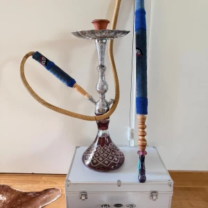 Vacker vattenpipa / shisha med en speciell slang - Elegant vattenpipa med en speciell och sällsynt slang, vackert mönstrad glasbas och detaljer i metall. Komplett med keramikskål och tillbehör. Ser ut att vara i mycket gott skick, inga synliga skador eller slitage. Perfekt för sociala tillfällen och avkoppling.