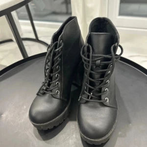 Svarta boots med klack från H&M Divided - Säljer ett par svarta boots från H&M Divided i storlek 37. Skorna har grov sula, hög klack och snörning framtill. Tillverkade i syntetmaterial med rund tå och robust känsla. Perfekta för dig som vill ha en edgy look.