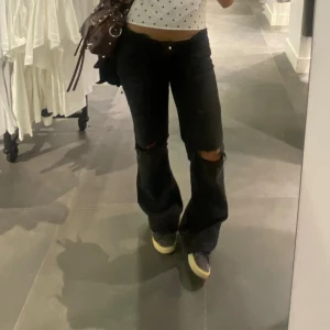 Svarta bootcut jeans med slitna knän - Svarta jeans från Nelly med bootcut passform och slitna hål på båda knäna. Klassiska femficksjeans med Nudie-signatur på bakfickorna. Knappt använd! 