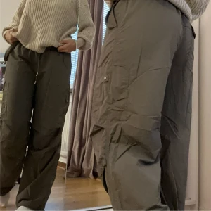 Gröna Parashoot med snörning - Säljer ett par gröna parashoot pants med bred passform och snörning i midjan. Byxorna har flera stora fickor på sidorna och är tillverkade i ett lätt och bekvämt material. Perfekta för en avslappnad och trendig look.