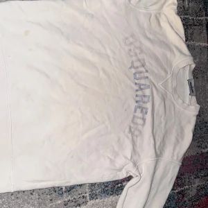 Vit sweatshirt från Dsquared2 - Vit sweatshirt från Dsquared2 med diskret blå logga över bröstet. Klassisk rund halsringning och långa ärmar. Tillverkad i mjuk bomull för en skön och avslappnad känsla. Perfekt för dig som gillar stilrena och enkla plagg.